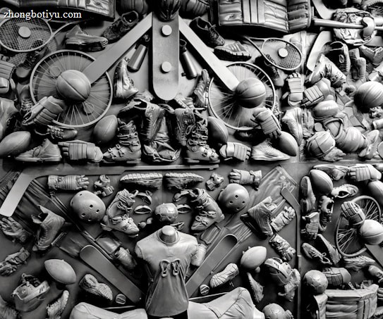 A complex arrangement of various sports equipment and attire, including tennis rackets, soccer balls, basketballs, helmets, shoes, gloves, and a mannequin torso wearing a T-shirt. The items are layered and artistically displayed in a monochrome color scheme, creating an intricate texture and visual pattern.